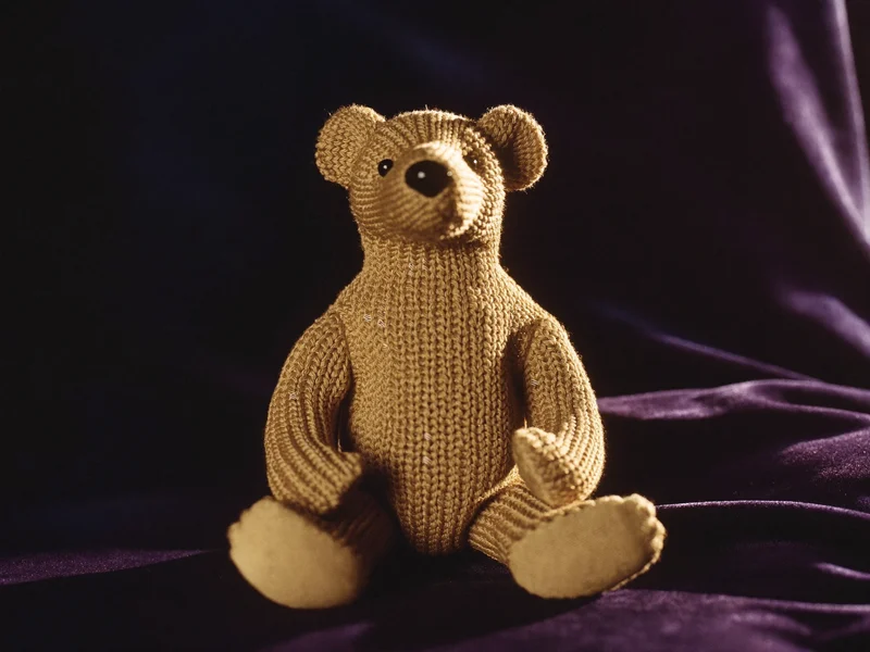 Ours en peluche tricotée assis sur un velours sombre, détail de la maille